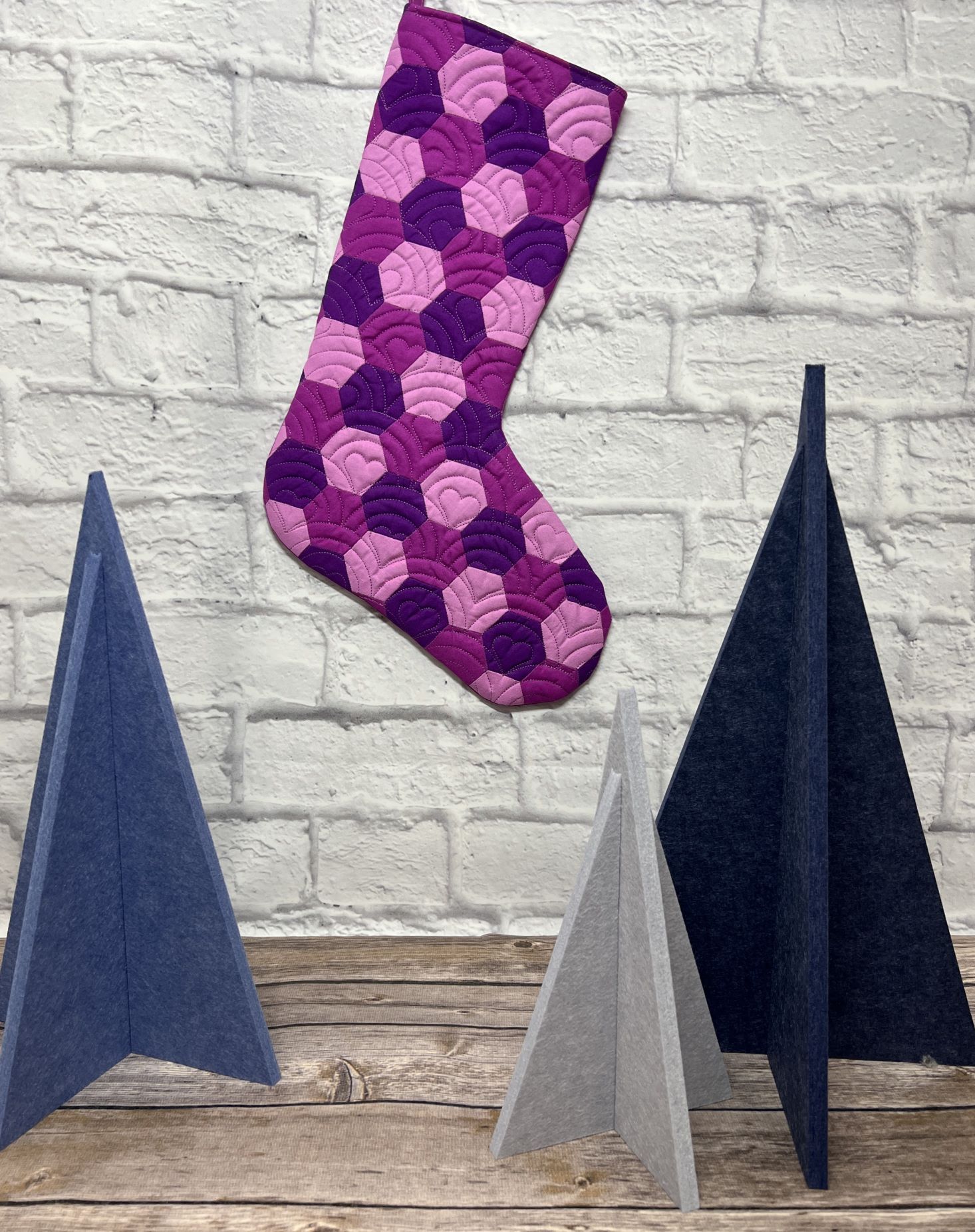 A purple stocking hanging on the wall next to two other stockings.